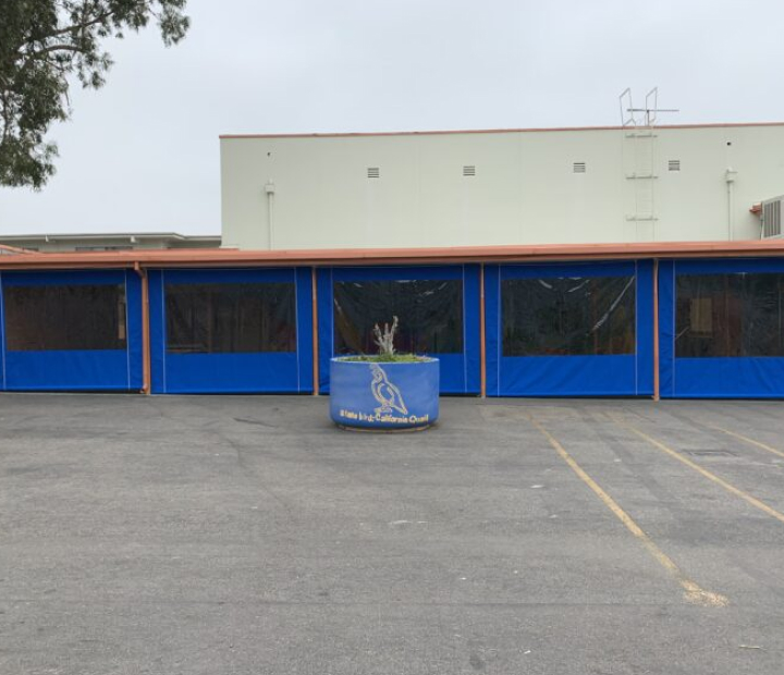 Blue outdoor curtain and screen panels enclosing a covered facility area